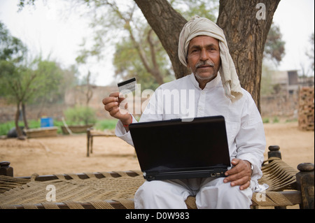 Farmer holding a credit card and using a laptop, Hasanpur, Haryana, India Stock Photo