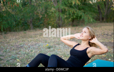 Athletic woman doing sit-ups to flex and strengthen her abdominal muscles on a mat in the park with copyspace Stock Photo