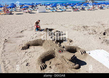 Artist making a sand sculpture of a giant crocodile or alligator on the beach of Playa Las Vistas in Los cristianos, Tenerife, Stock Photo