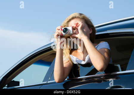 Woman photographer leaning out of car window taking a photo with a compact digital camera Stock Photo