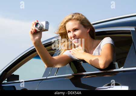 Attractive blonde woman tourist leaning out taking photographs from a car window Stock Photo