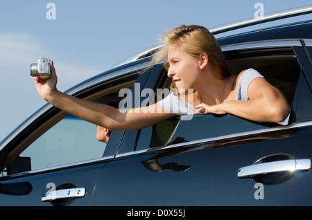 Low angle view of an attractive female tourist leaning out of the window and photographing from car Stock Photo
