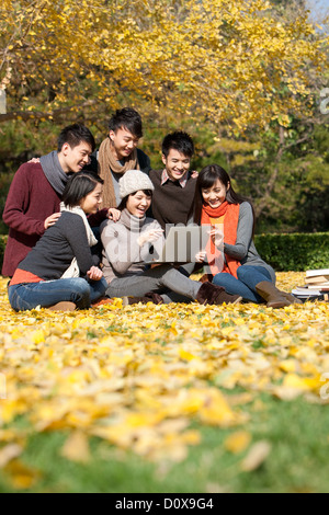 Cheerful college students with laptop and books on campus in a beautiful autumn day Stock Photo