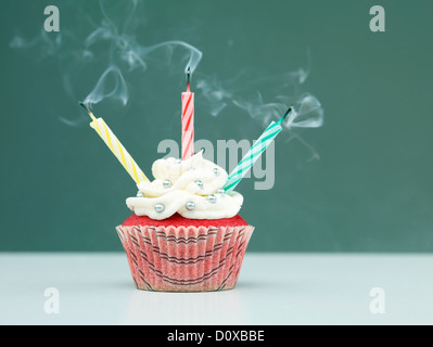 muffin on the table with three lit candles on blue background blown Stock Photo