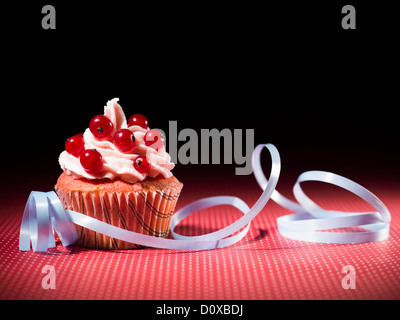 muffin with red currants on a table decorated with blue ribbons dotted red and black background Stock Photo