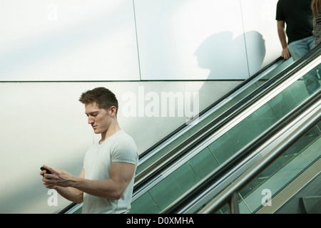 Young man on escalator using smartphone Stock Photo