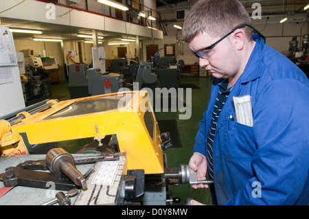 Young white man in blue overalls on a factory floor on an engineering apprenticeship wearing protective safety glasses operating a machine Stock Photo