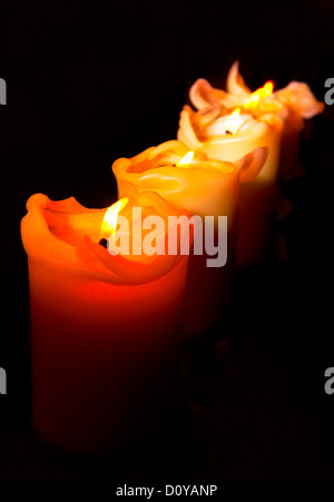 Four candles in a row, all lit and against a black background Stock Photo