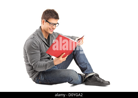 Smiling guy sitting on a floor and reading a book isolated on white background Stock Photo