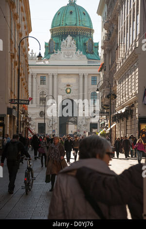 Green dome and white facade of Hofburg Palace at end of pedestrian street as people in coats walk in the pale autumn sunlight. Stock Photo