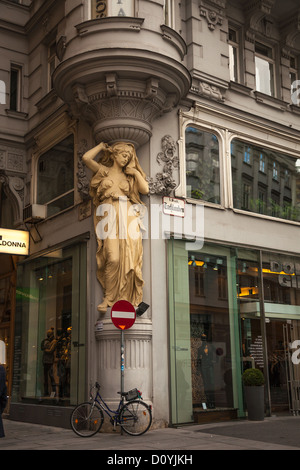 Bicycle parked outside a shop beneath an Art Deco sculpture of a woman holding up the decorative corner of a building in Vienna. Stock Photo