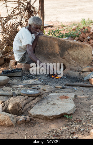 Old rural indian village man metalworking at a small outside furnace. Andhra Pradesh India Stock Photo