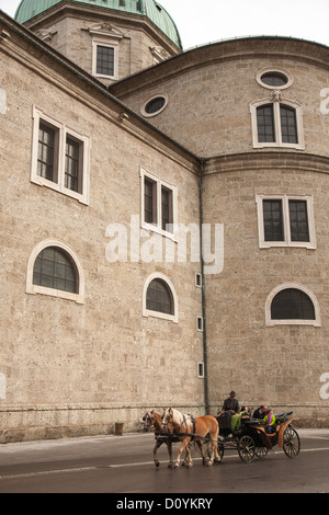 A horse and carriage takes family of tourists for a ride around Salzburg's Residenzplatz, past the high stone walls of the Dom. Stock Photo