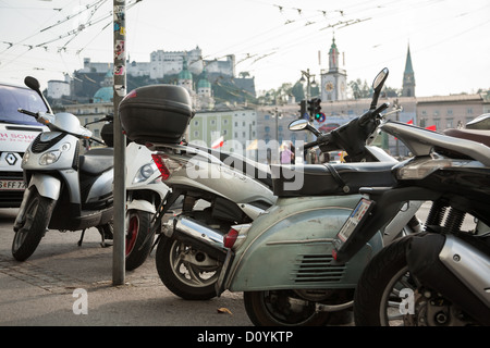 Scooters parked on the sidewalk in Salzburg with the city behind and the historic Festung Hohensalzburg high above. Stock Photo