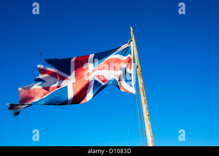 Ragged, torn and neglected Union Jack, the British national flag, on a flag pole against a clear blue sky. Stock Photo