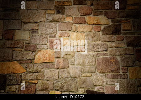Masonry wall of multicolored stone blocks lit from above Stock Photo