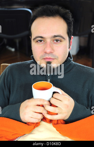 Young man in blanket holding cup of tea Stock Photo