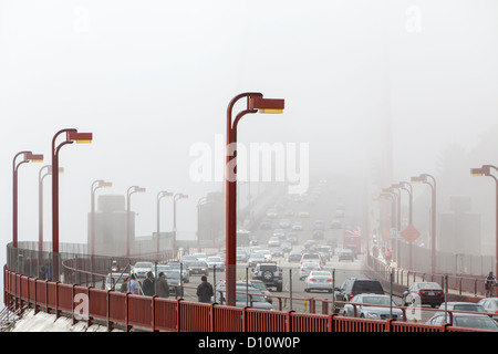 The San Francisco Golden Gate Bridge covered in fog and pedestrians walking across the bridge and cars driving across. Stock Photo