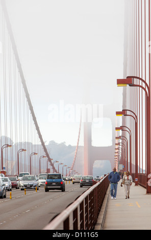 The San Francisco Golden Gate Bridge covered in fog and pedestrians walking across the bridge and cars driving across. Stock Photo