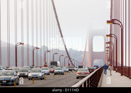 The San Francisco Golden Gate Bridge covered in fog and pedestrians walking across the bridge and cars driving across. Stock Photo