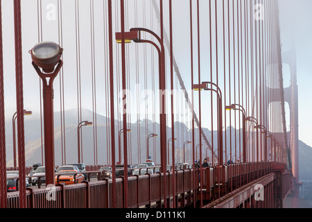 The San Francisco Golden Gate Bridge covered in fog and pedestrians walking across the bridge and cars driving across. Stock Photo