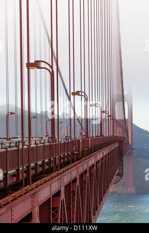 The San Francisco Golden Gate Bridge covered in fog and pedestrians walking across the bridge and cars driving across. Stock Photo