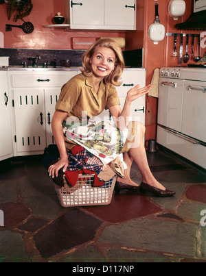 1960s YOUNG SMILING BLOND HOUSEWIFE SITTING ON TOP OF LAUNDRY BAS pic