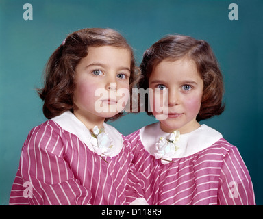 1960s PORTRAIT TWIN SISTERS WEARING PINK STRIPED DRESSES LOOKING AT CAMERA Stock Photo