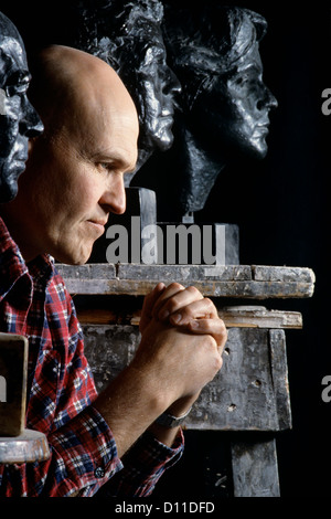 1980s MAN ARTIST HANDS CLASPED THINKING PRAYING SURROUNDED BY SCULPTURES Stock Photo
