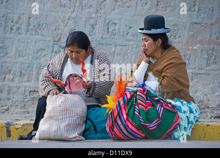 Two Aymara women in traditional dress and with shopping bags sitting on footpath in the city of La Paz, Bolivia, South America Stock Photo