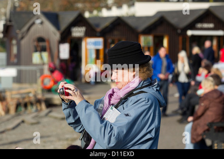 Woman tourist  taking photograph using a digital compact came on Bowness Bay front  on Lake Windermere Stock Photo