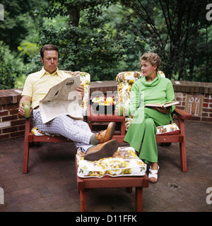1970s COUPLE MAN WOMAN MIDDLE AGED SITTING PATIO DECK READING BOOK NEWSPAPER RETRO Stock Photo