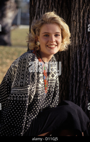 1990s BLONDE WOMAN WEARING SWEATER SITTING NEAR TREE SMILING LOOKING AT CAMERA Stock Photo