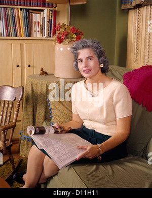 1960s MIDDLE AGED WOMAN READING HOLDING OPEN MAGAZINE SMILING SITTING LOOKING AT CAMERA Stock Photo