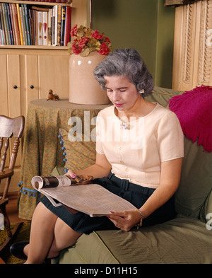 1960s MIDDLE AGED WOMAN SITTING READING HOLDING OPEN MAGAZINE Stock Photo