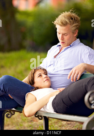 Young woman lying on her boyfriend's lap sitting on a park bench Stock Photo