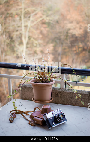 Vintage soviet analog camera (fed-5v) with a brown leather case, put on a white balcony table. Autumn colours in the background Stock Photo