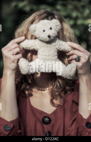 a woman is hiding behind a white teddy bear Stock Photo