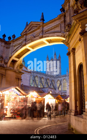 Christmas Market stalls seen through arch with Bath Abbey in the background at night / twilight / dusk Bath Somerset England UK Stock Photo