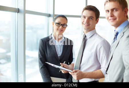 Image of three employees looking at camera, focus on elegant man with clipboard Stock Photo