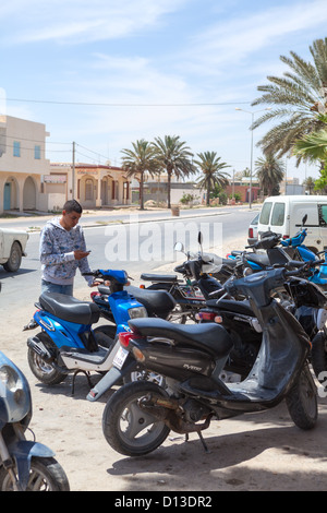 Teenager with phone standing near the scooter, Tunisia, Africa Stock Photo