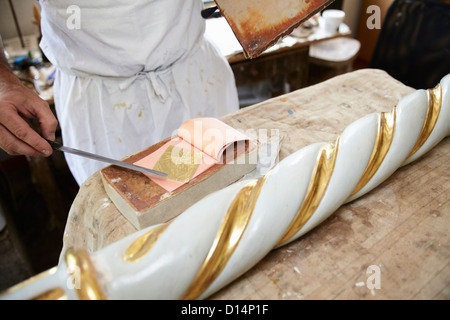 Worker applying gold leaf to pole Stock Photo