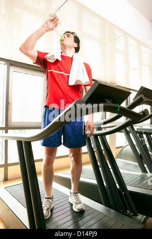 Man drinking water on treadmill at gym Stock Photo