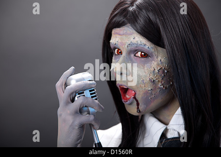 Cute zombie girl singer with retro microphone, studio shot  Stock Photo