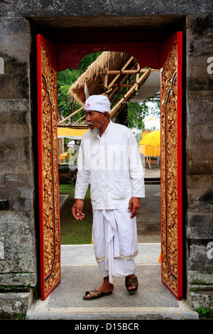 Hindu priest entering a Temple through an ornately decorated door. Pura Dalem Tengaling Temple at Pejeng. Near Ubud, Bali Stock Photo