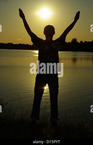 A man stands on against a sun with heaved up hands Stock Photo