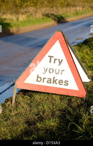 A Try Your Brakes warning sign sitting on a grass verge near a flooded road in Norfolk. Stock Photo
