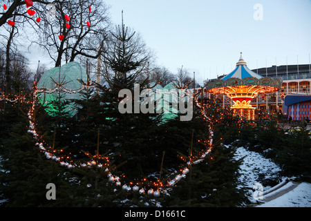 Merry-go-round, Christmas trees and decorations at dusk at the Christmas market in the snow covered Tivoli, Copenhagen, Denmark Stock Photo