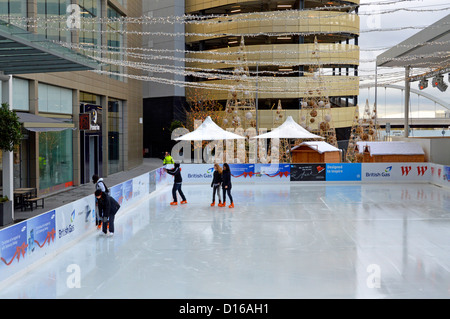 People using skating rink at the Westfield shopping centre complex with multi storey public car park beyond Stratford Newham East London England UK Stock Photo