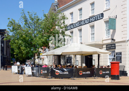 People relaxing outside the Saracens Head Hotel sitting in shade provided by large white parasol Chelmsford town centre High Street Essex England UK Stock Photo